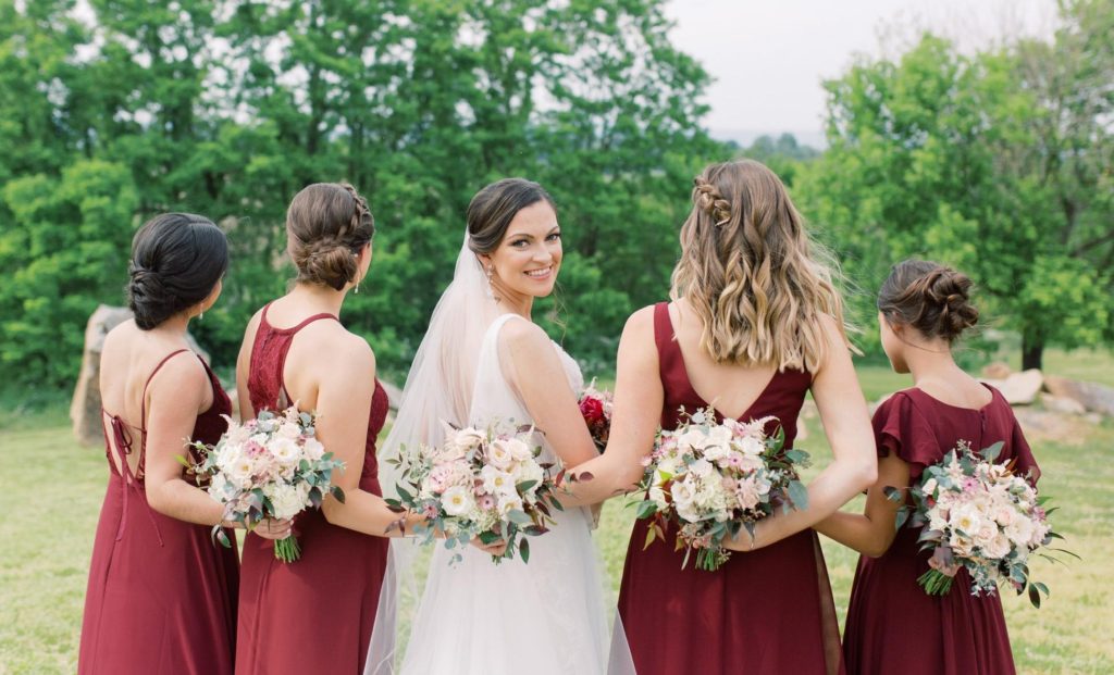 bride looking back at camera with bridesmaids wearing maroon dresses for Timeless Wedding AYS blog