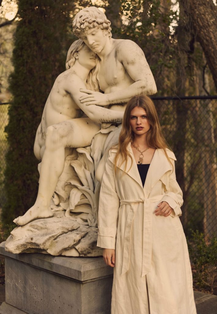 woman in cream trench coat standing in front of marble statue