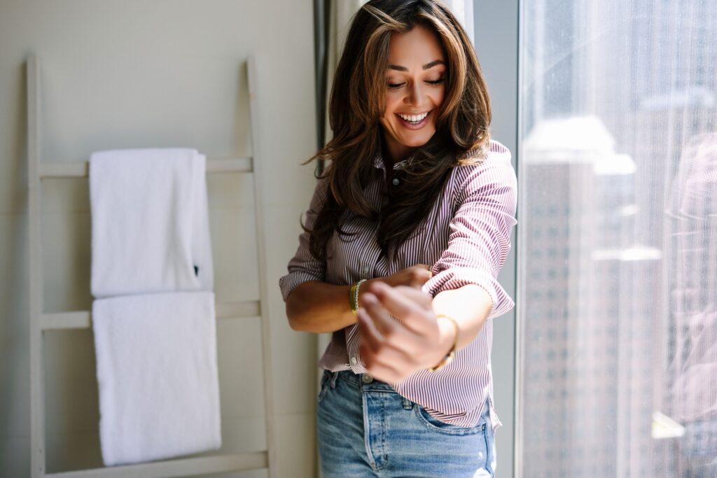 woman rolling sleeves up with layered color hair and big smile, gold wath and mid rise jeans find signature style