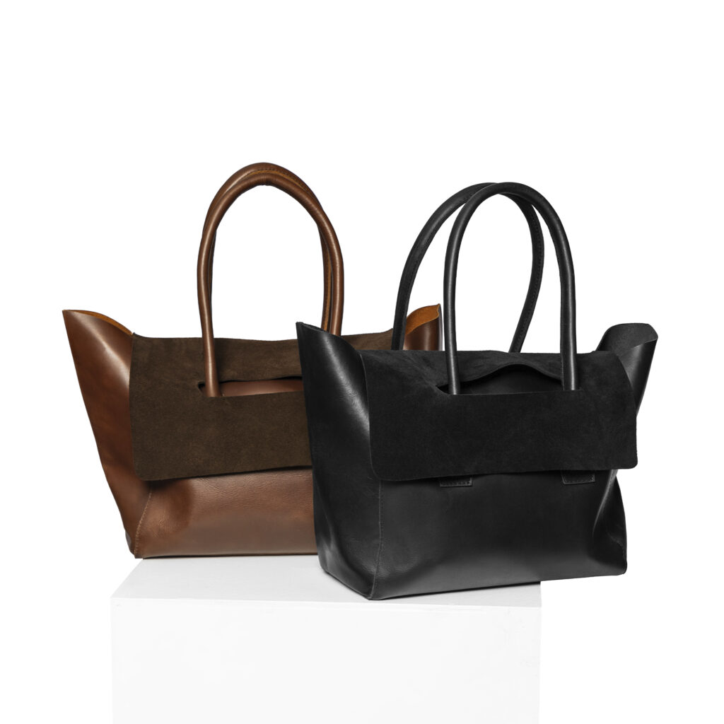 Two structured tote bags, one in brown leather and the other in black leather, both with suede accents and top handles, are displayed on a white surface against a white background.
