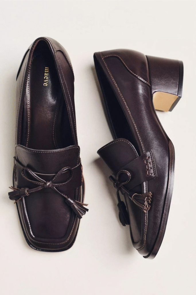 A pair of dark brown leather loafers with a square toe, a decorative bow with tassels, and a block heel.