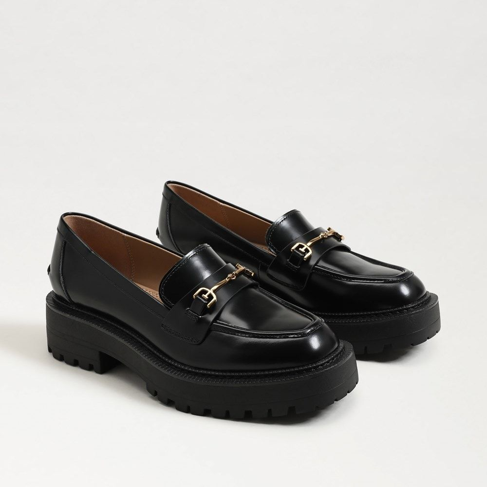 A pair of black leather loafers with a gold buckle detail and a thick lug sole.