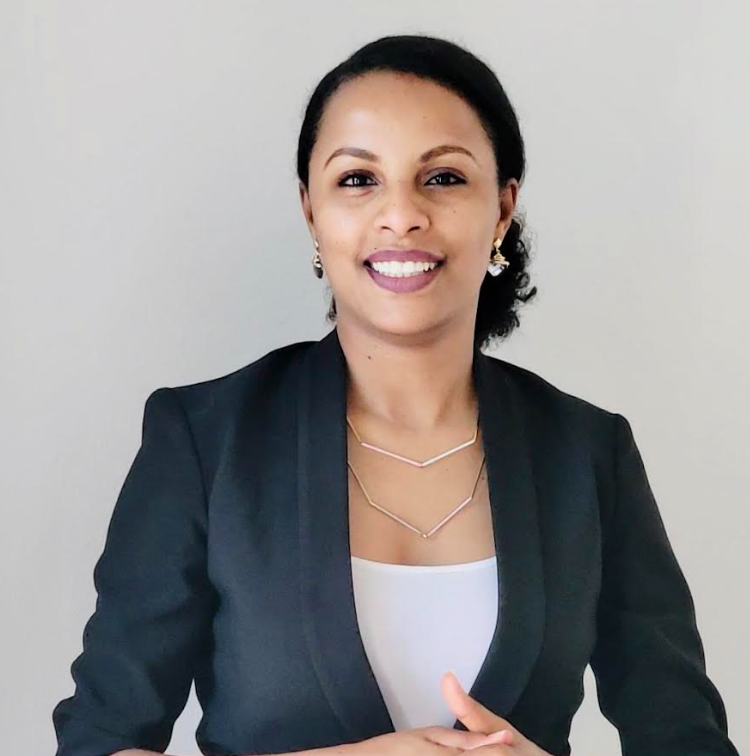 Hiwot in a black blazer and white top smiles at the camera, wearing a layered necklace and earrings.